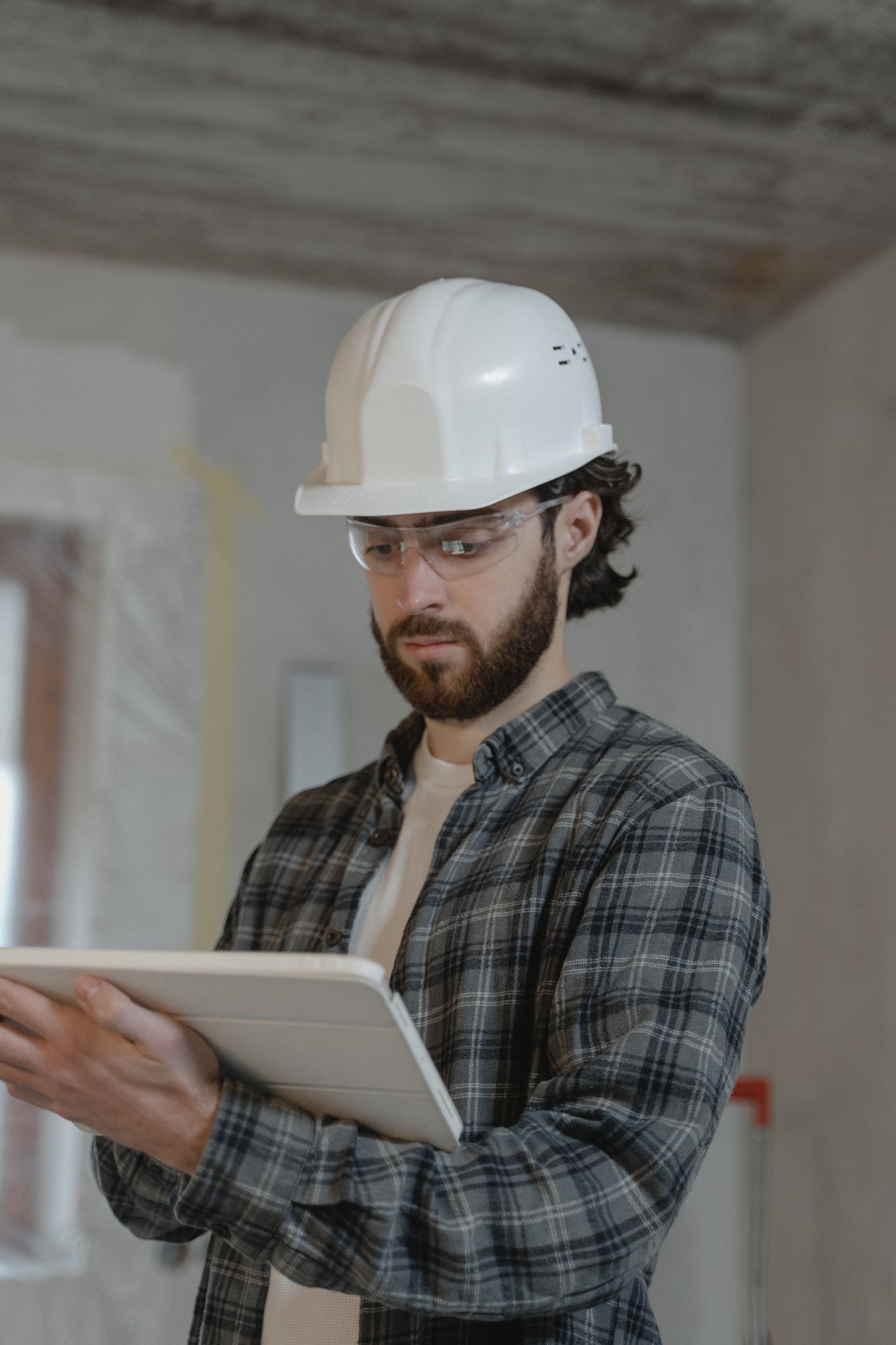 A general contractor in a hard hat checking plans on a tablet inside a renovation